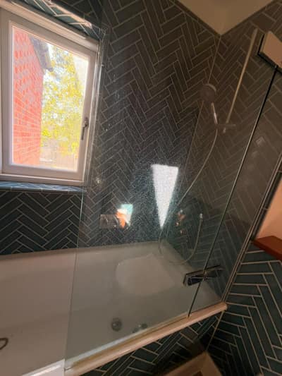 Bath with a gleaming glass screen and teal herringbone tiles
