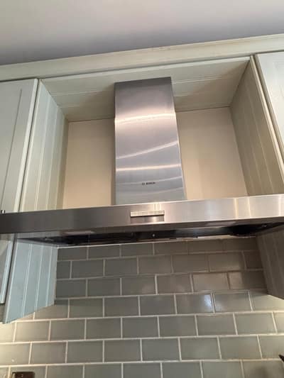 Stainless steel cooker hood above a tiled splashback